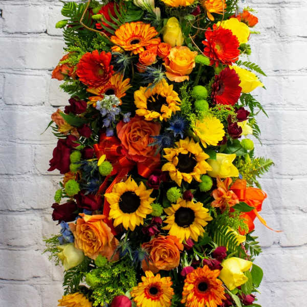 Tall arrangement of sunflowers, roses, and gerbera daisies in bright mixed colors