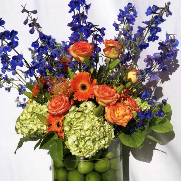 Orange roses and gerbera daisies in a vase with blue flowers