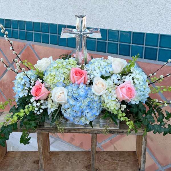 Floral arrangement with roses and hydrangeas around a clear glass cross