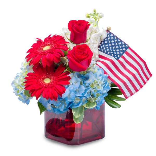 Patriotic arrangement with red roses, red gerberas, blue hydrangeas and a US flag in a red glass cube vase