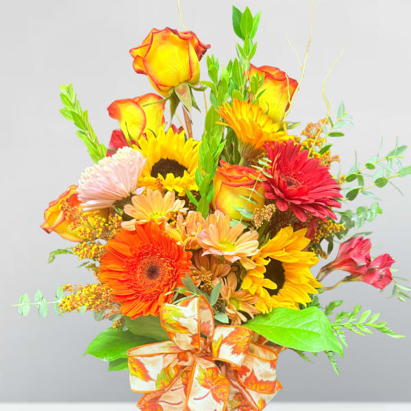 Bouquet of mixed autumn flowers in a glass vase with a patterned ribbon
