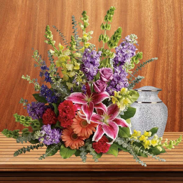 Mixed bouquet with lilies, roses, and purple blooms beside a decorative urn