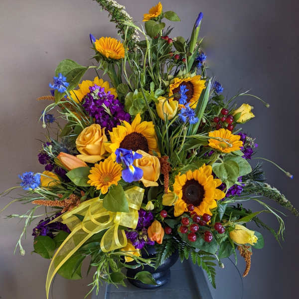 Large mixed bouquet with sunflowers, yellow roses, and purple flowers in a black vase