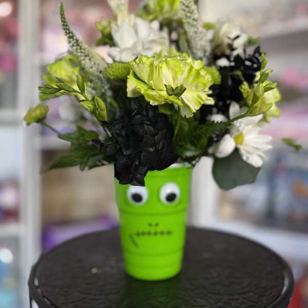 Bouquet of green, white, and black flowers in a bright green cup with eyes