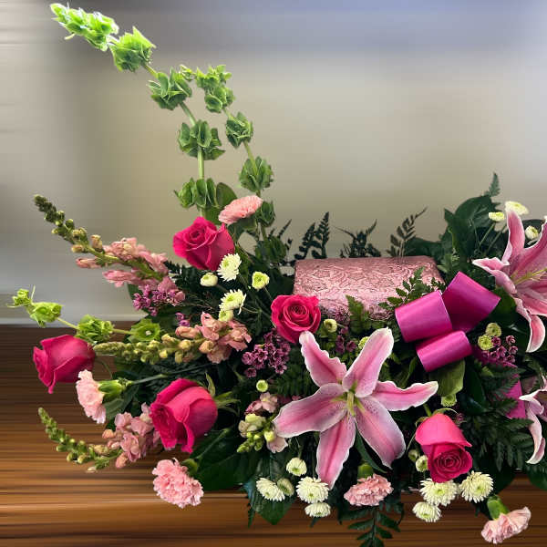 Pink lilies and roses arranged around a pink keepsake box with Bells of Ireland accents