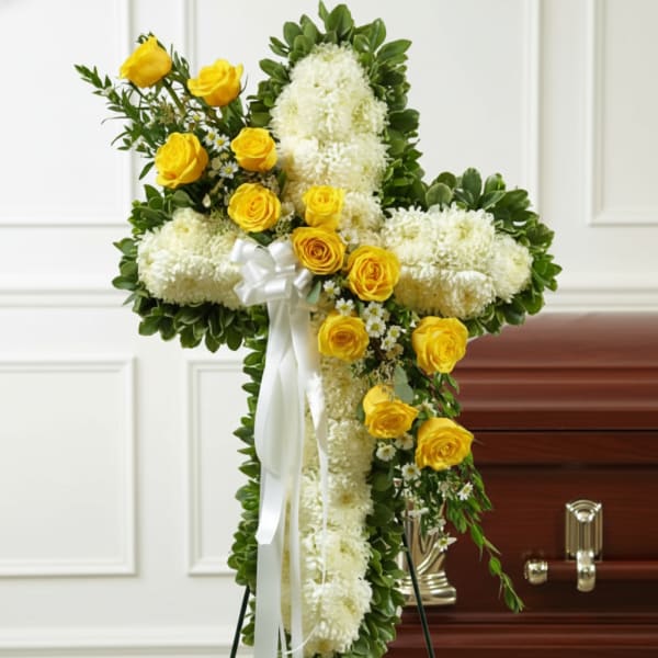 White floral cross with yellow roses and ribbon on a stand