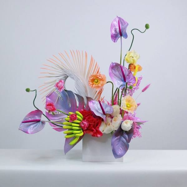 Colorful floral arrangement in a white square vase with purple anthuriums