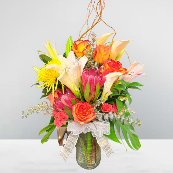 Mixed bouquet with roses, lilies, and protea in a glass vase