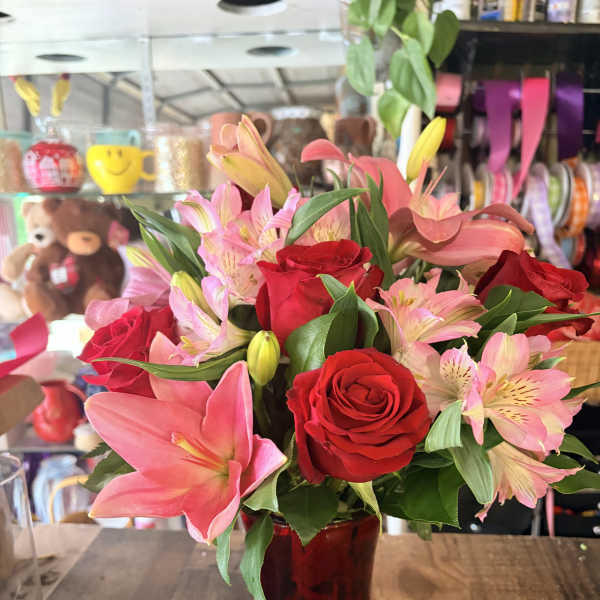 Bouquet of red roses and pink lilies in a red glass vase