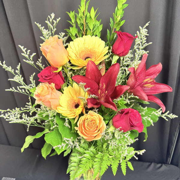 Mixed bouquet of roses, gerbera daisies, and lilies in a glass vase