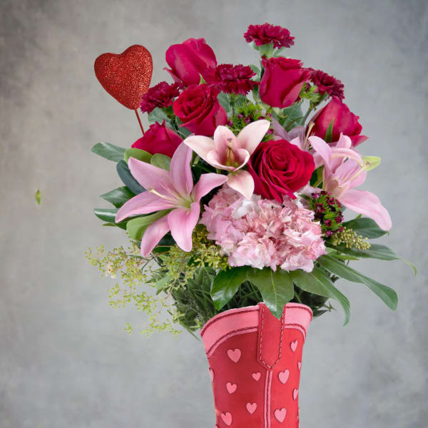 Pink and red flower arrangement in a heart-decorated cowboy boot vase