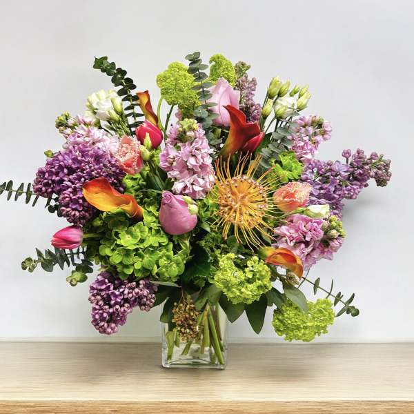 Mixed bouquet in a clear glass vase with pink, purple, green, and orange flowers