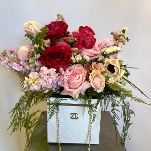 Mixed pink and red roses arranged in a white box with trailing greenery