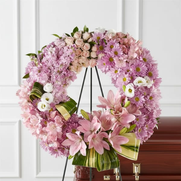 Pink floral funeral wreath on a stand with lilies and daisies