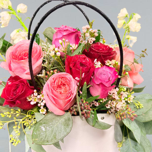 Pink and red roses arranged in a white basket with black handles