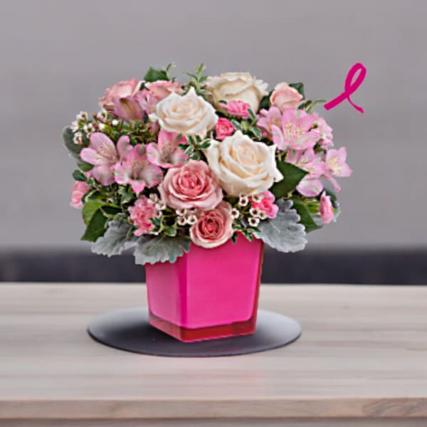 Pink and white floral arrangement in a bright pink vase with a ribbon accent