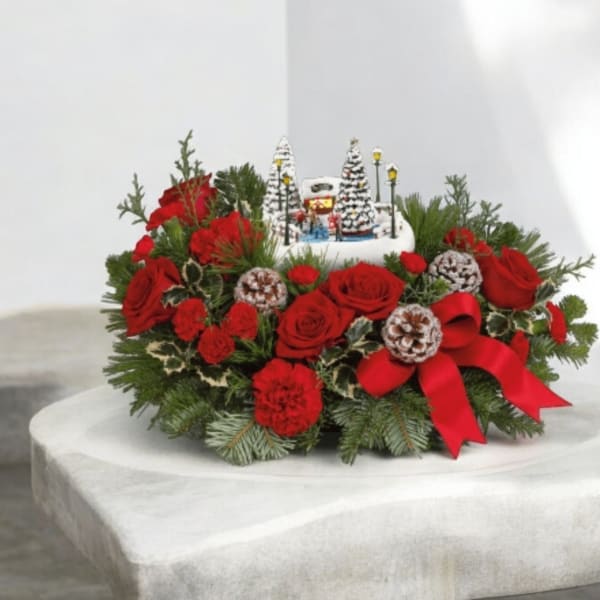 Red roses and pine arranged around a small winter village centerpiece