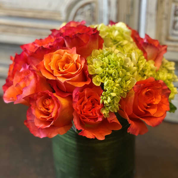 Orange and red roses with green hydrangeas in a glass vase