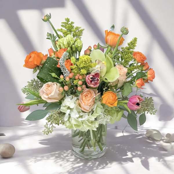 Mixed bouquet of orange, peach, pink, and green flowers in a glass vase