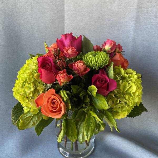 Bouquet of pink and orange roses with green hydrangeas in a glass vase