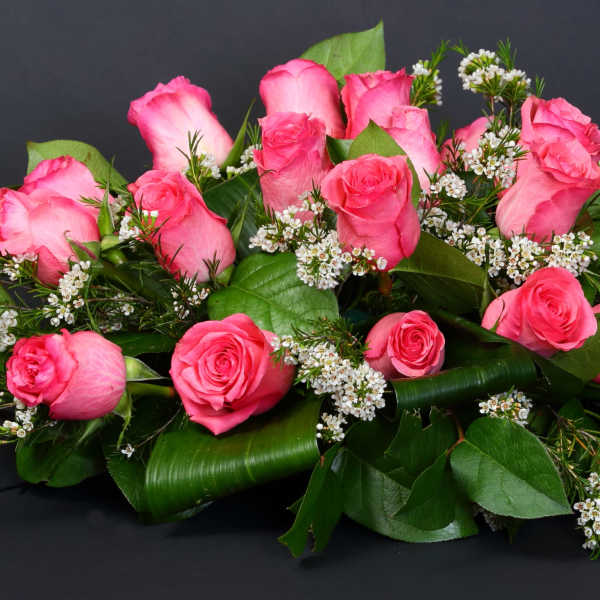 Pink roses arranged with small white filler flowers and greenery