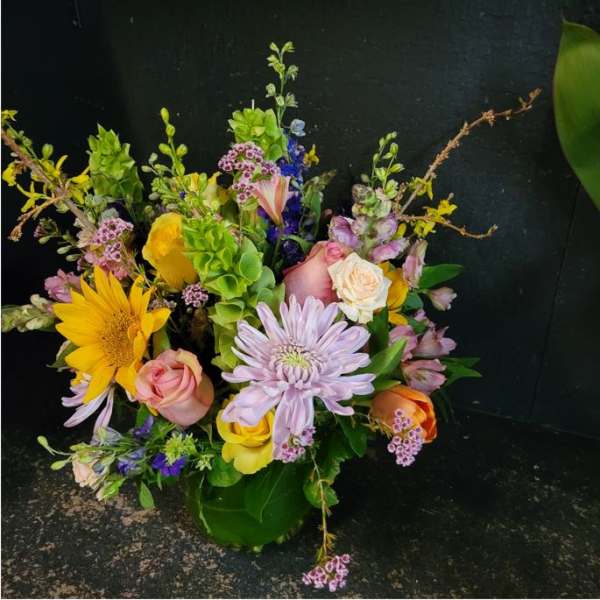 Mixed bouquet with yellow sunflower, pink roses, and lavender blooms in a green vase