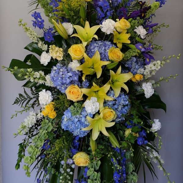 Large standing floral spray with yellow lilies, blue hydrangeas, and yellow roses
