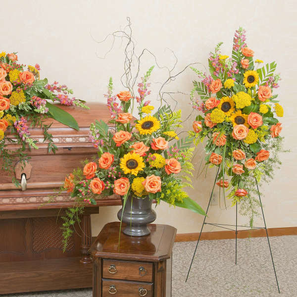 Sympathy set with orange roses and yellow sunflowers on a casket, in a vase, and on a standing spray.