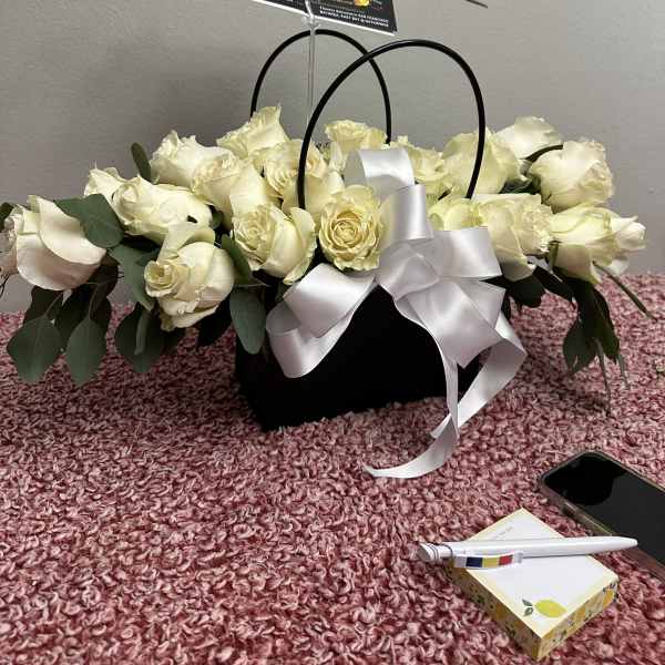 White rose arrangement in a black basket with a white ribbon and card pick