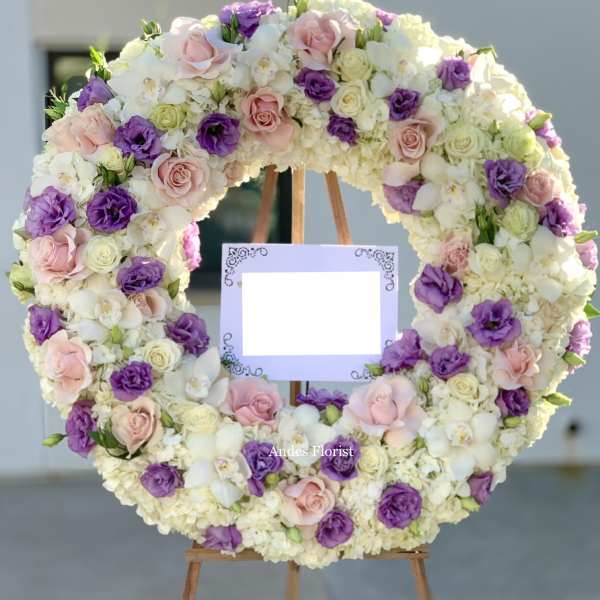 Large floral wreath of pink, purple, and white blooms on an easel with a blank sign