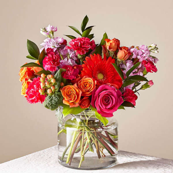 Mixed bouquet of pink, orange, and red flowers in a clear glass vase
