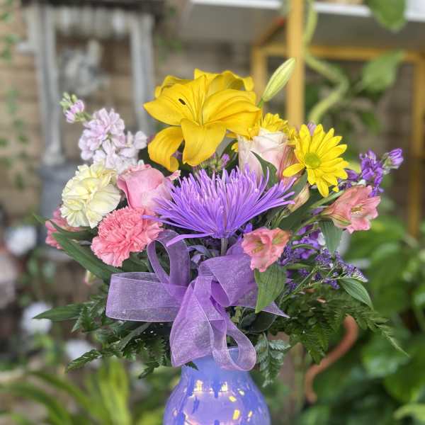 Mixed bouquet of yellow, purple, pink, and white flowers in a lavender vase
