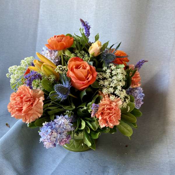 Mixed bouquet of orange roses, carnations, and purple flowers in a green vase