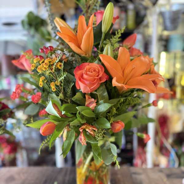 Orange lilies and roses in a clear glass vase