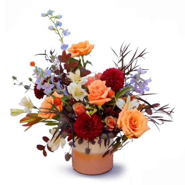 Orange roses and red blooms in a ceramic vase