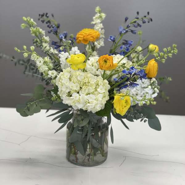Mixed yellow, white, and blue flowers arranged in a glass vase