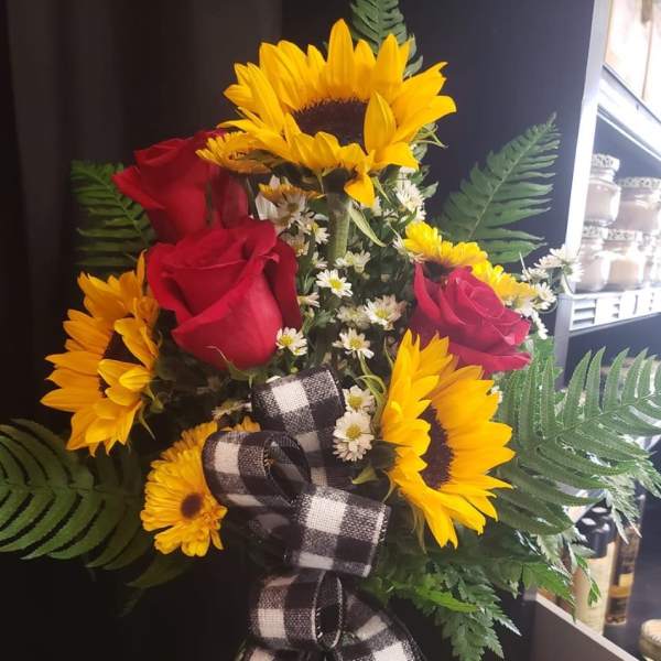Bouquet of sunflowers and red roses in a glass vase with a plaid ribbon