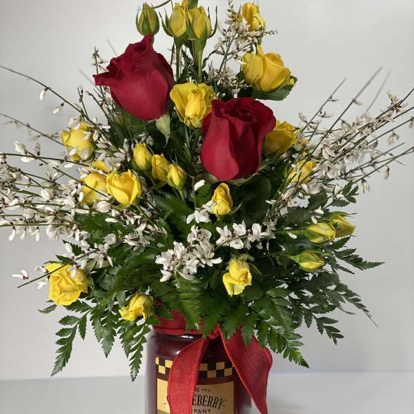 Red and yellow roses in a glass jar with a red ribbon