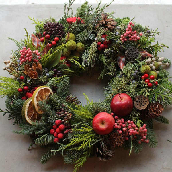 Holiday wreath with evergreen branches, red berries, apples, and pinecones