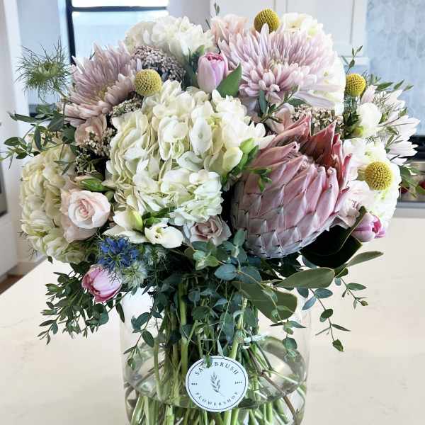 Mixed bouquet of pale pink, white, and lavender flowers in a glass vase