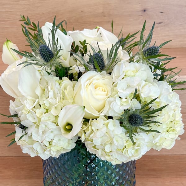 White roses and hydrangeas in a blue glass vase with spiky blue thistles