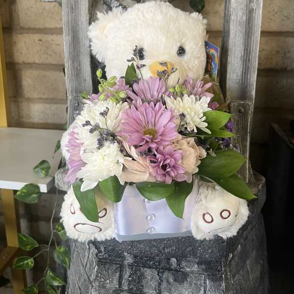 Teddy bear holding a pastel flower arrangement in a box