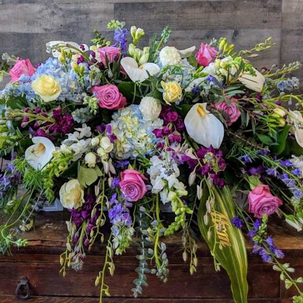 Low elongated arrangement of mixed pink, white, yellow, and blue flowers on a wooden surface