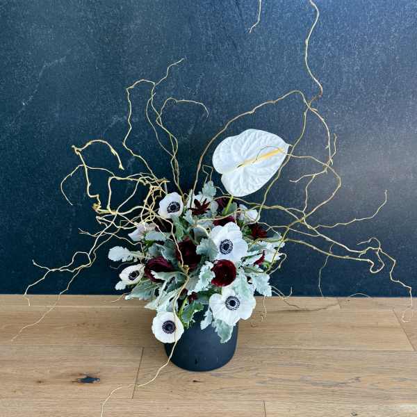White anemones and dark red blooms in a black vase with curly branches