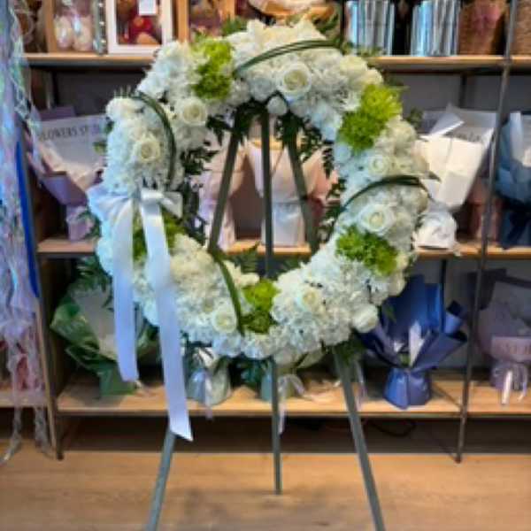 White floral wreath on a stand with a white ribbon
