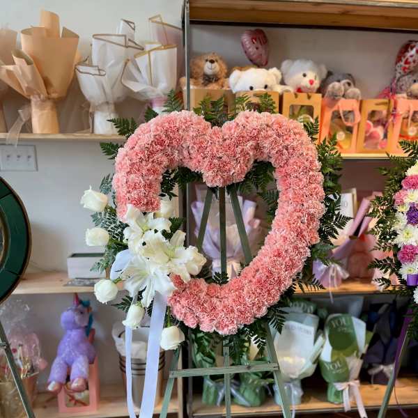 Pink carnation heart wreath on an easel with white lilies and ribbon