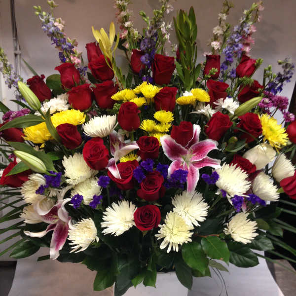 Large mixed bouquet of red roses, lilies, and white chrysanthemums in a white container