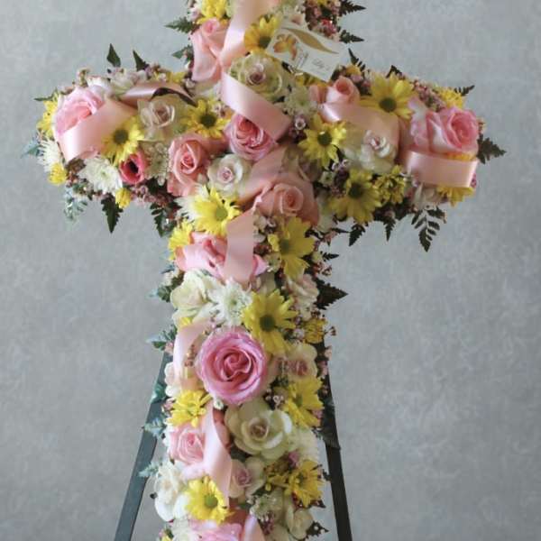 Cross-shaped floral arrangement with pink roses and yellow daisies on an easel