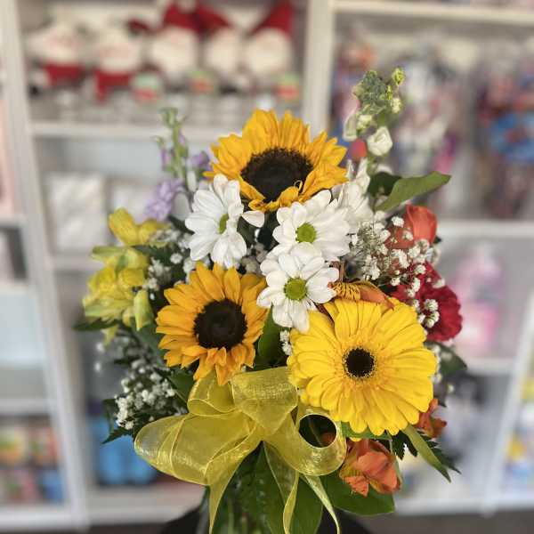 Mixed bouquet with sunflowers, white daisies, and a yellow ribbon in a glass vase