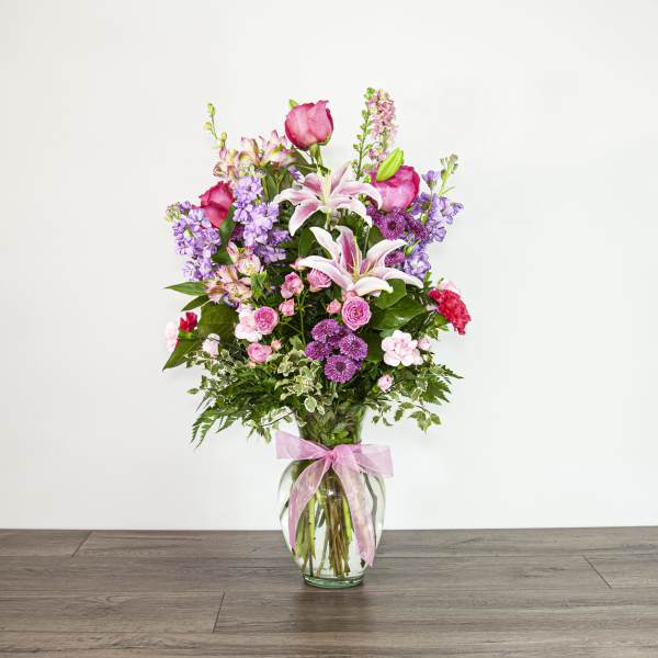 Tall bouquet of pink and purple flowers in a glass vase with a pink ribbon